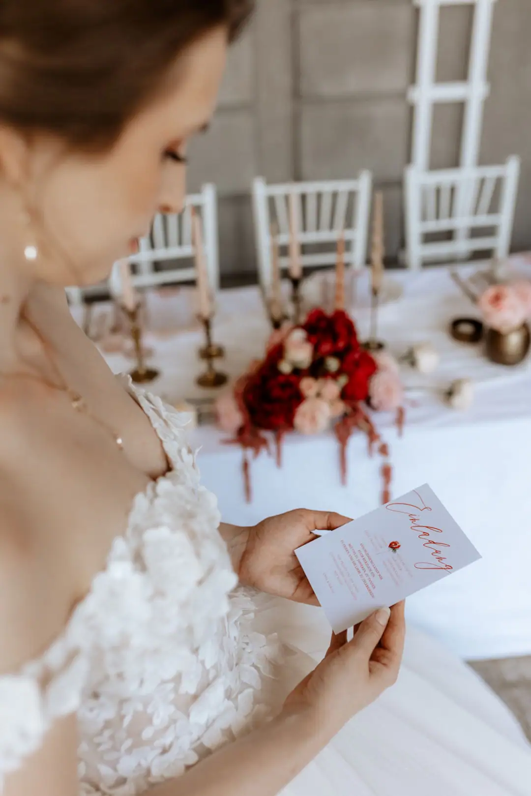 Braut bewundert ihre Einladungskarte in Rot, Weiß und Blush, passend zu ihrer Hochzeitslocation, Deko und Blumen