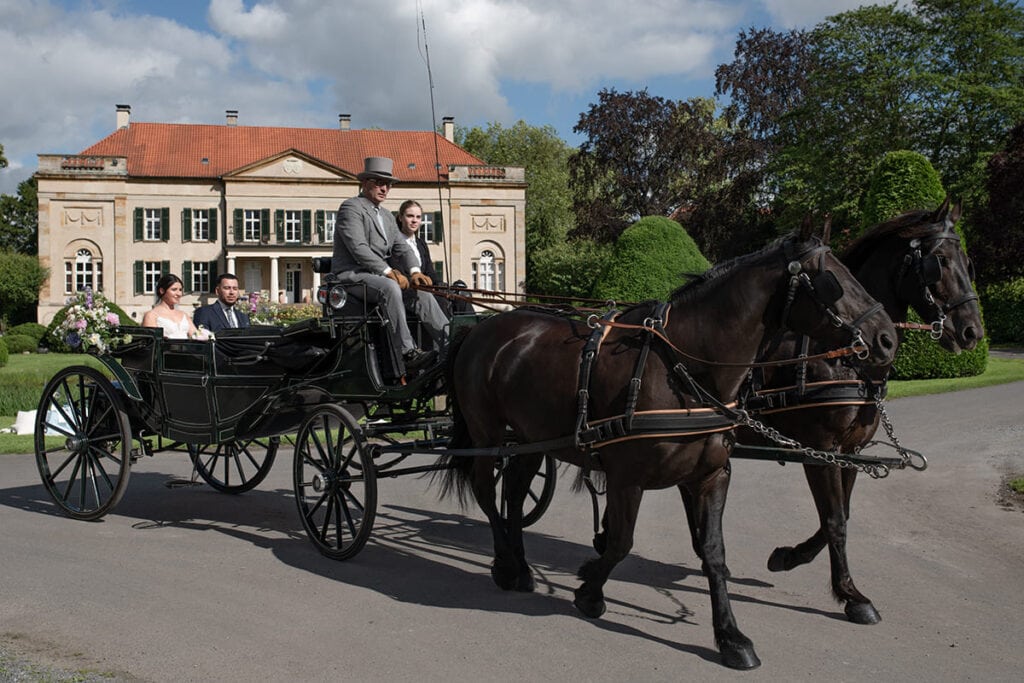 Brautpaar fährt in historischer Pferdekutsche vor Schloss Harkotten vor