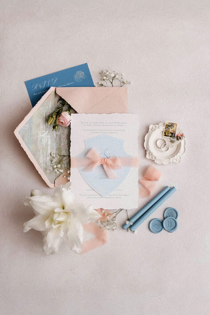 Hochzeitseinladung mit rosafarbener Seidenschleife, hellblauen Wachssiegeln und Monet-Kuvertfutter