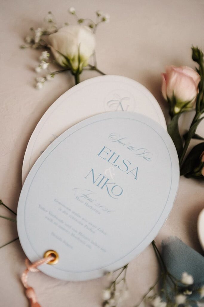 Ovale Save-the-Date-Karten in Hellblau mit Monogramm und Kordel-Anhänger