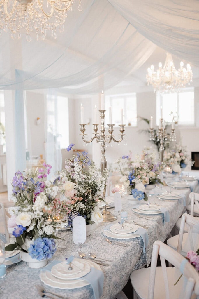Festlich gedeckte Hochzeitstafel mit Kronleuchtern, Kerzenlicht und pastellfarbenem Blumenschmuck